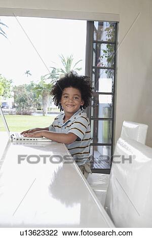 Stock Image - Boy (5-6 years) using laptop in dining room portrait. Fotosearch