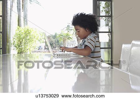 Boy (5-6 years) using laptop in dining room side view View Large Photo Image Stock Photo - Boy (5-6 years) using laptop in dining room side view. Fotosearch
