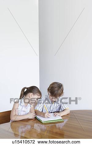 Stock Image - Boy (7-9) and girl (5-6) doing homework together. Fotosearch