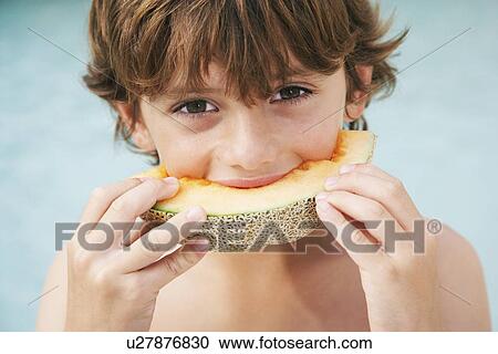 Stock Image - Boy (7-9) eating slice of melon close-up. Fotosearch