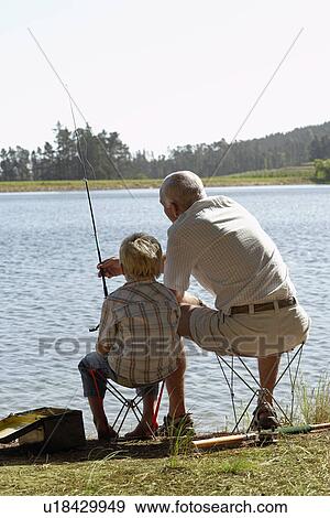 Stock Photo - Boy (7-9) fishing with grandfather back view.. Fotosearch