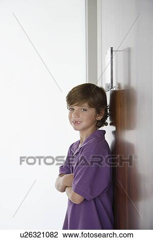 Stock Image - Boy (7-9) leaning on wardrobe and smiling. Fotosearch