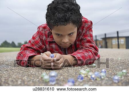 Boy (7-9) playing marbles lying in playground View Large Photo Image Stock Image - Boy (7-9) playing marbles lying in playground. Fotosearch