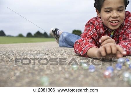 Boy (7-9) playing marbles lying in playground View Large Photo Image Stock Photograph - Boy (7-9) playing marbles lying in playground. Fotosearch