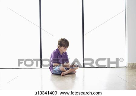 Boy (7-9) sitting on floor playing handheld game View Large Photo Image Stock Photo - Boy (7-9) sitting on floor playing handheld game. Fotosearch