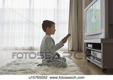 Stock Image - Boy (7-9) sitting on floor watching cartoons in television. Fotosearch
