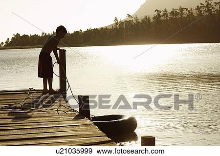 Stock Photo - Boy (7-9) standing on dock pulling in float tube. . Fotosearch