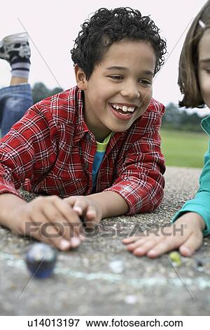 Stock Photo - Boy and girl (7-9) playing marbles in playground. Fotosearch