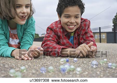Boy and girl (7-9) playing marbles lying in playground View Large Photo Image Stock Photo - Boy and girl (7-9) playing marbles lying in playground. Fotosearch
