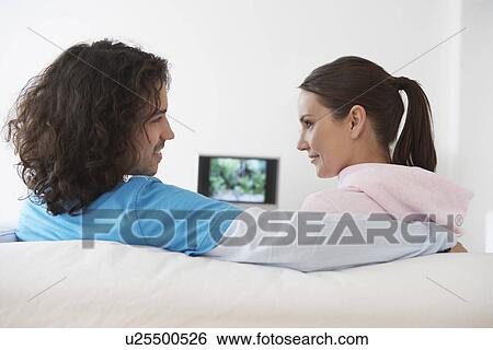 Stock Photograph - Boyfriend and girlfriend sitting on sofa looking in eyes back view. Fotosearch