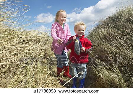 Stock Photo - Brother and sister (4-6) standing among long grass. Fotosearch