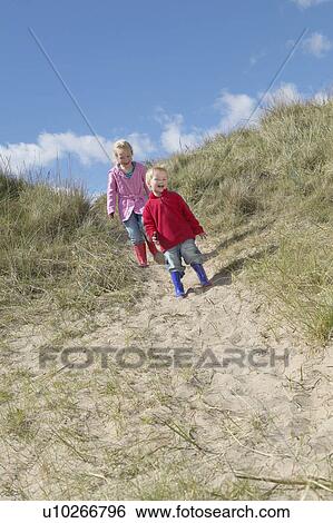 Stock Photograph - Brother and sister (4-6) standing on sand dunes. Fotosearch