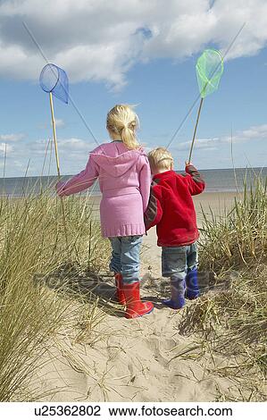 Brother and sister (4-6) with fishing nets standing on sand dunes View Large Photo Image Stock Image - Brother and sister (4-6) with fishing nets standing on sand dunes. Fotosearch