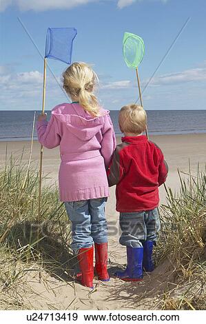 Brother and sister (4-6) with fishing nets standing on sand dunes View Large Photo Image Stock Photo - Brother and sister (4-6) with fishing nets standing on sand dunes. Fotosearch