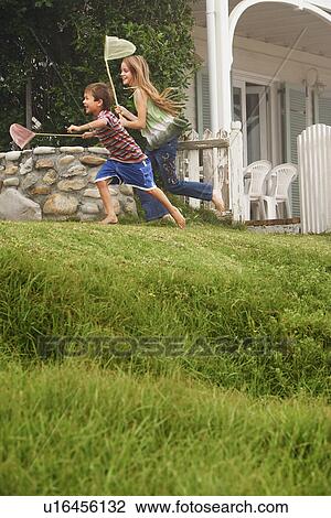 Stock Image - Brother and sister (5-6 10-12) holding fishing nets running in front of house. Fotosearch