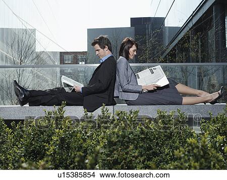 Picture - Business man and woman sitting back to back on wall outdoors reading newspapers side view. Fotosearch