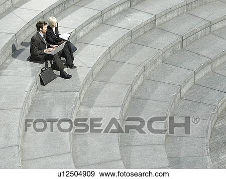 Stock Photo - Business man and woman sitting on spiral stairs using laptop elevated view. Fotosearch