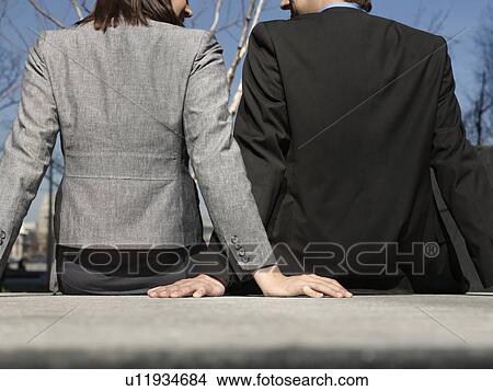 Business man and woman sitting on wall outdoors back view (cropped) View Large Photo Image Picture - Business man and woman sitting on wall outdoors back view (cropped). Fotosearch