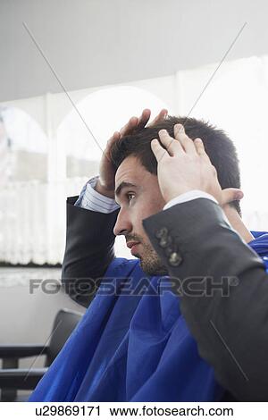 Stock Image - Business man checking freshly cut hair in barbers. Fotosearch