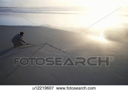 Stock Photo - Business man drawing arrow in sand on beach elevated view. Fotosearch