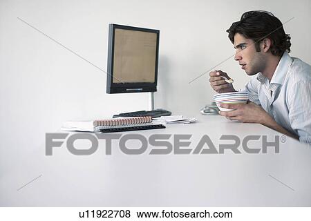 Business man eating sitting at office desk side view View Large Photo Image Stock Photo - Business man eating sitting at office desk side view. Fotosearch