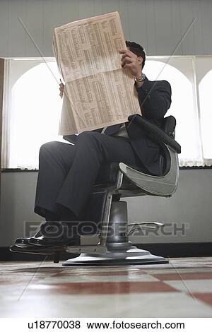 Stock Photo - Business man reading newspaper waiting in barber shop. Fotosearch