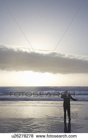 Stock Photo - Business man using mobile phone standing in sea at sunset elevated view. Fotosearch