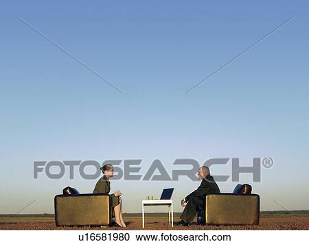 Stock Image - Business people sitting in chairs on open plain. Fotosearch