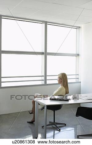Stock Photo - Business woman looking through window sitting in office. Fotosearch
