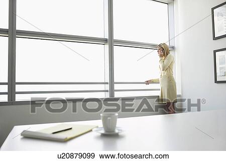 Business woman using mobile phone standing by window in office side view View Large Photo Image Stock Photo - Business woman using mobile phone standing by window in office side view. Fotosearch