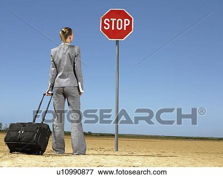 Business woman with luggage standing in front of stop sign in desert back view View Large Photo Image Stock Photo - Business woman with luggage standing in front of stop sign in desert back view. Fotosearch