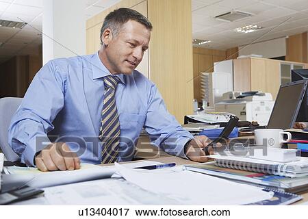 Businessman dialling cell phone at desk View Large Photo Image Stock Photo - Businessman dialling cell phone at desk. Fotosearch