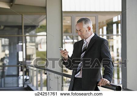 Stock Image - Businessman leaning on railing using mobile phone.. Fotosearch
