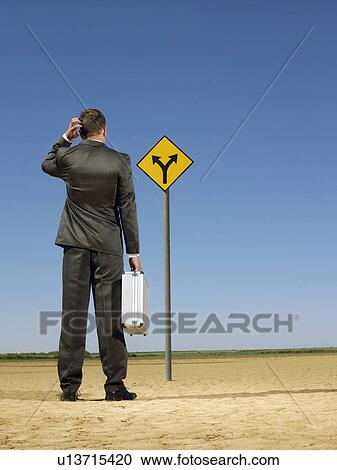 Businessman looking at road sign in desert back view View Large Photo Image Stock Image - Businessman looking at road sign in desert back view. Fotosearch