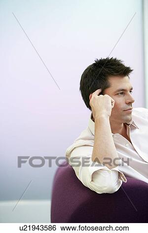 Stock Photograph - Businessman reclining hand on head on sofa side view. Fotosearch