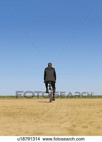 Businessman riding bicycle in desert back view View Large Photo Image Picture - Businessman riding bicycle in desert back view. Fotosearch