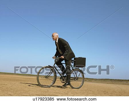 Stock Photography - Businessman riding bicycle in desert. Fotosearch