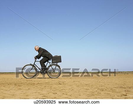 Stock Photography - Businessman riding bicycle in desert. Fotosearch