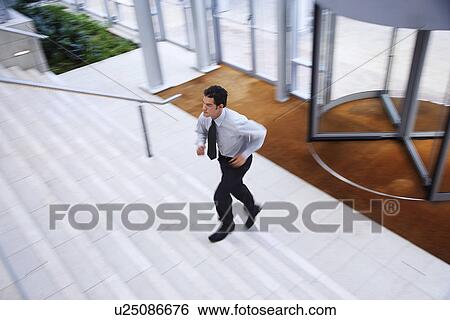 Stock Photograph - Businessman running up stairs in office lobby. Fotosearch