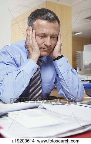 Businessman sitting at desk with head in hands View Large Photo Image Picture - Businessman sitting at desk with head in hands. Fotosearch