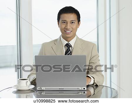Stock Photography - Businessman sitting at table working on laptop portrait. Fotosearch
