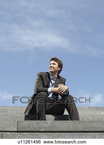 Stock Photograph - Businessman sitting on steps outdoors low angle view. Fotosearch
