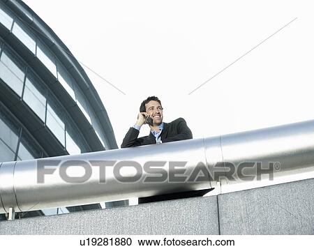 Businessman standing behind pipe outside office building using mobile phone low angle view View Large Photo Image Stock Image - Businessman standing behind pipe outside office building using mobile phone low angle view. Fotosearch