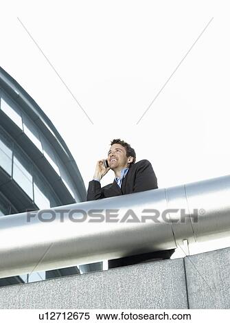 Businessman standing behind pipe outside office building using mobile phone low angle view View Large Photo Image Stock Photography - Businessman standing behind pipe outside office building using mobile phone low angle view. Fotosearch