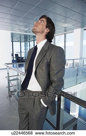 Stock Photo - Businessman standing in office corridor looking up. Fotosearch
