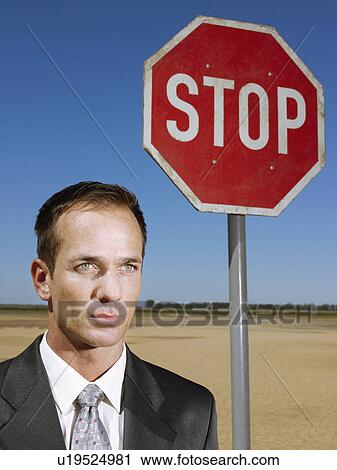 Businessman standing next to stop sign in desert head and shoulders View Large Photo Image Stock Image - Businessman standing next to stop sign in desert head and shoulders. Fotosearch
