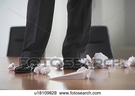 Stock Photo - Businessman standing on conference table with crumpled paper low section. Fotosearch