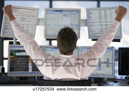 Picture - Businessman watching computer screens with arms raised back view.. Fotosearch