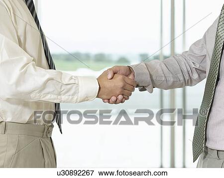 Stock Photo - Businessmen Shaking Hands in front of window side view close-up. Fotosearch