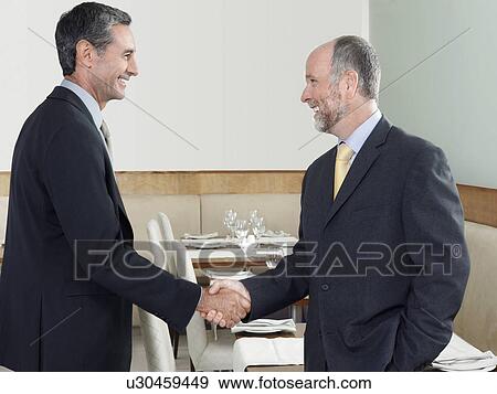 Stock Photo - Businessmen shaking hands in restaurant. Fotosearch